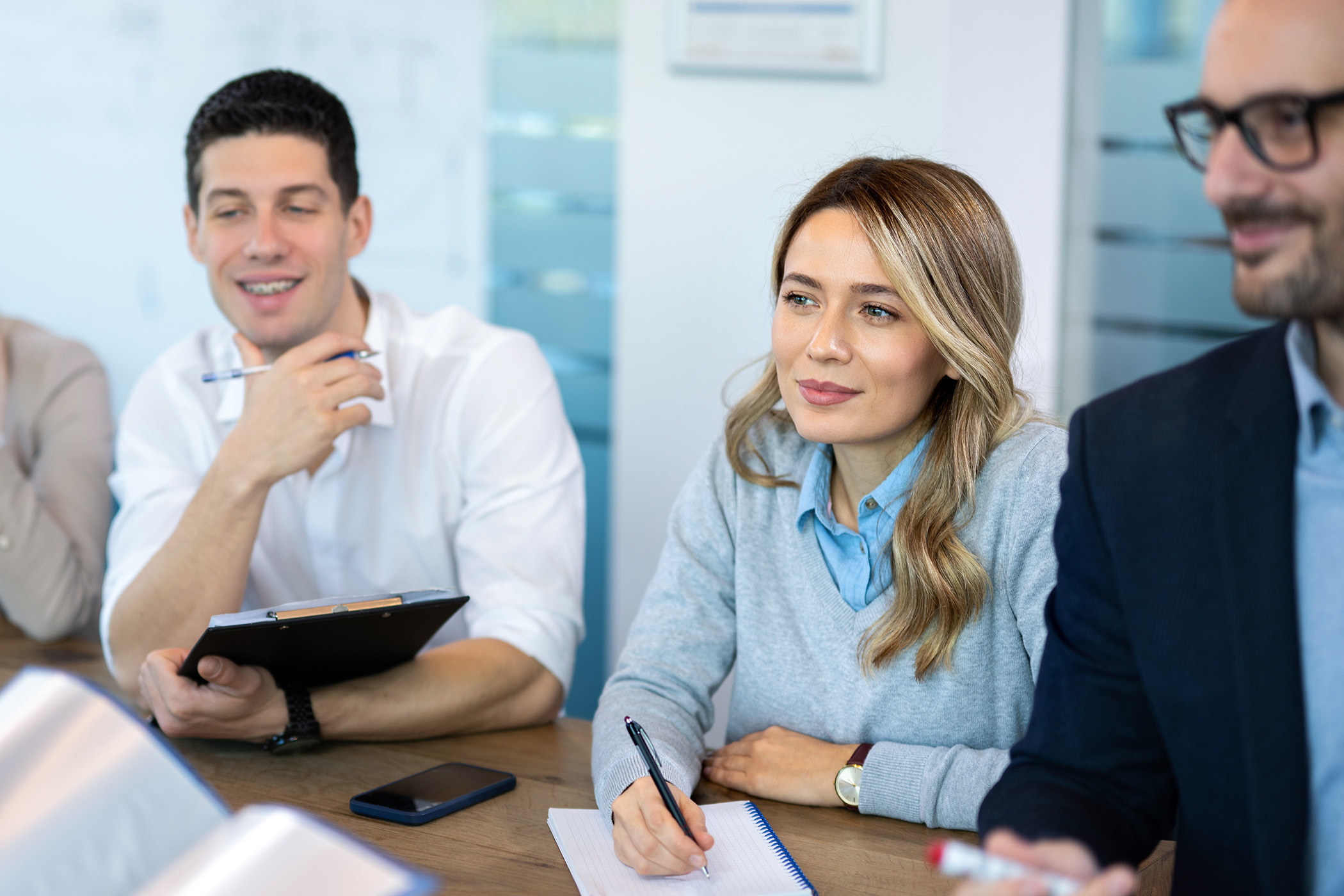 Konferenzmeeting im Büro - Eine Frau lächelt in die Kamera während sie Notizen macht.