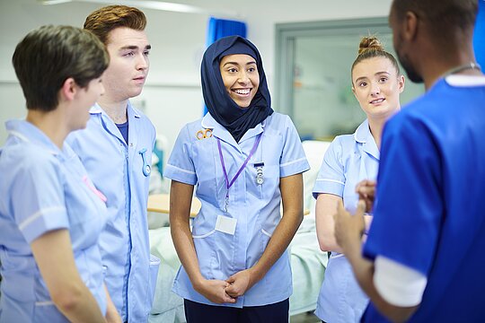 Foto: Pflegepersonal im Krankenhaus mit fünf Personen, teiweise mit Kopftuch, verschiedener Hautfarbe, männglich und weiblich