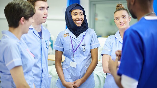 Foto: Pflegepersonal im Krankenhaus mit fünf Personen, teiweise mit Kopftuch, verschiedener Hautfarbe, männglich und weiblich