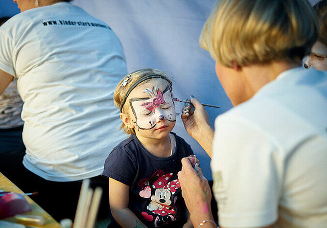 Foto: Einem Kind wird gerade ein Schmetterling aufs Gesicht geschminkt