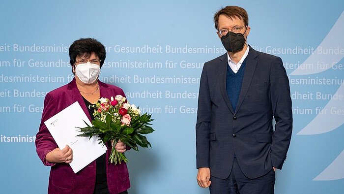 Bundesgesundheitsminister Prof. Dr. Karl Lauterbach mit der Pflegebeauftragen Claudia Moll (beide mit Masken), Moll mit Blumenstrauß und Ernennungsurkunde in den Händen