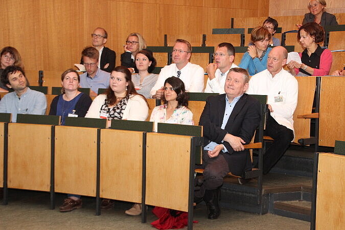 Foto: Bundesgesundheitsminister Gröhe und weitere Zuhörer/-innen sitzen in einem Hörsaal mit Tribüne