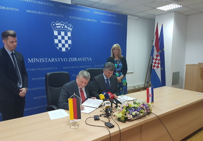 Foto: Bundesgesundheitsminister Hermann Gröhe und sein Amtskollege Milan Kujundžić sitzen an einem langen, hellen Tisch mit Mikrofonen und unterschreiben die Erklärung; im Hintergrund ist ein blau-weißes Banner an der Wand mit dem kroatischen Wappen und der Aufschrift "Ministarstvo Zdravstva", daneben sind die kroatische und die europäische Flagge aufgestellt