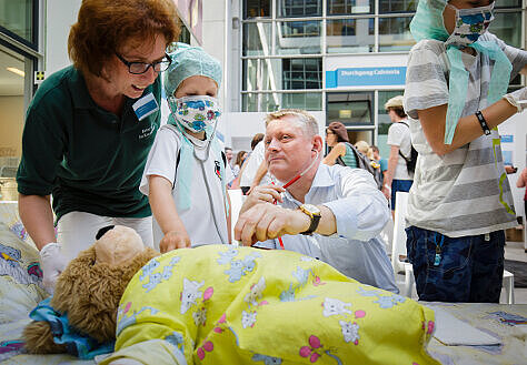 Minister Gröhe und ein Kind untersuchen den kranken Teddy Bruno