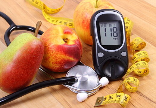 Foto: Ein Blutzuckermessgerät, ein Stethoskop und ein Maßband liegen neben Obst auf einem Tisch 