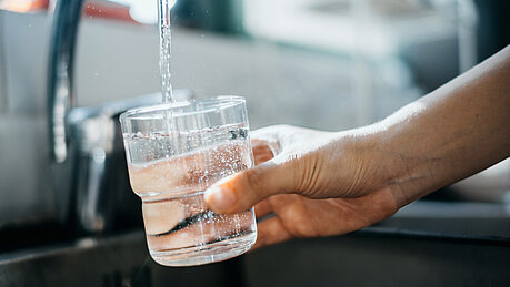 Nahaufnahme einer Hand, die ein Glas mit Wasser direkt aus dem Wasserhahn in der Küchenspüle füllt