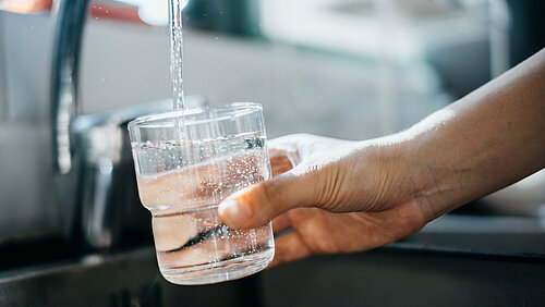 Nahaufnahme einer Hand, die ein Glas mit Wasser direkt aus dem Wasserhahn in der Küchenspüle füllt