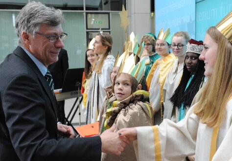 Foto: Auf einer kleinen Bühne im Bundesgesundheitsministerium stehen die Sternsinger; Staatssekretär Lutz Stroppe schüttelt einer Sternsingerin die Hand