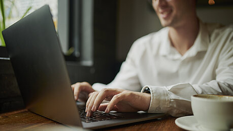 Eine Person sitzt an einem Tisch und tippt auf einem Laptop