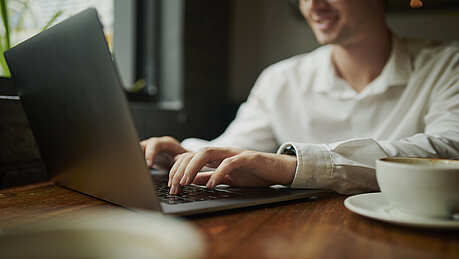 Eine Person sitzt an einem Tisch und tippt auf einem Laptop