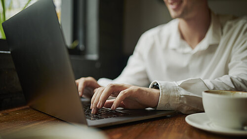 Hands, person and journalist with laptop at cafe for research, creative writing and editing article. Man, typing and online with coffee for closeup, communication and story information of publication