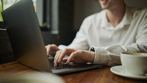 Hands, person and journalist with laptop at cafe for research, creative writing and editing article. Man, typing and online with coffee for closeup, communication and story information of publication