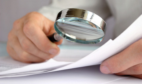 Gutachten (Bildquelle: sergign/Shutterstock) Foto: Jemand hält in einer Hand ein Blatt Papier, das er durch eine Lupe betrachtet, die er in der anderen Hand hält