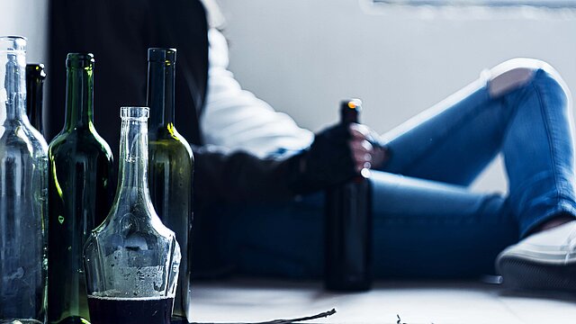 Person umgeben von Alkoholflaschen