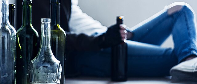 Person umgeben von Alkoholflaschen