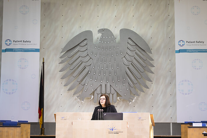 Foto: Dr. Ruth Hecker bei ihrer Eröffnungsrede, im Hintergrund der Bundesadler