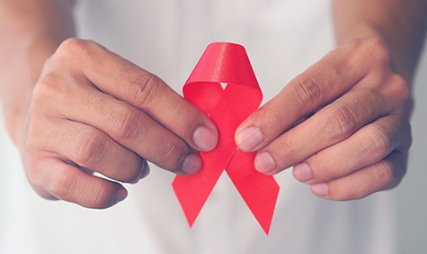 Zwei Hände umfassen eine rote Schleife (Bildquelle: Teechai/Shutterstock.com) Zwei Hände umfassen eine rote Schleife.