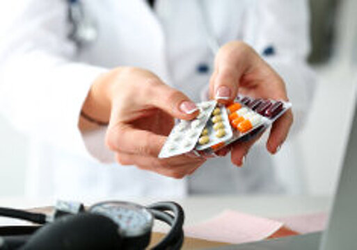 Foto: Eine Frau in weißem Kittel hält eine Auswahl an unterschiedlichen Tabletten in Blister-Verpackungen in der Hand 