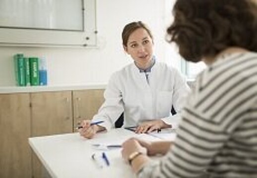 Foto: Patientin im Gespräch mit einer Ärztin, am Tisch sitzend