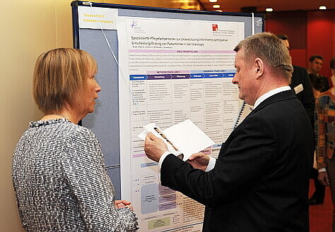 Foto: Minister Gröhe vor einem Schaubild im Gespräch mit einer Teilnehmerin