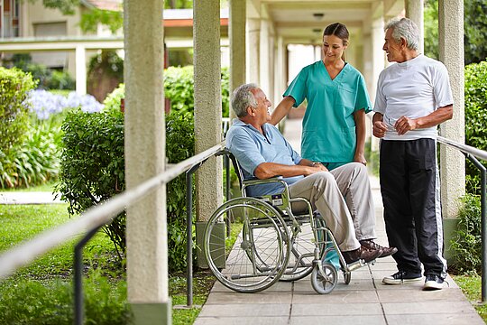 Ein Patient im Rollstuhl unterhält sich mit einer Krankenpflegerin und einem Mitpatienten