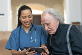 Eine Pflegekraft zeigt einem älteren Herrn was auf einem iPad
