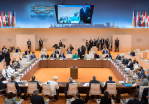 photo: view into the conference room of the G20 summit; participants sitting around a table, a video screen and flags of the country in the background