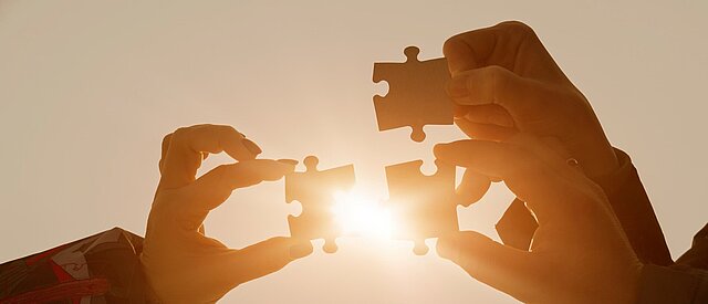 Drei Hände halten Puzzleteile in die Sonne