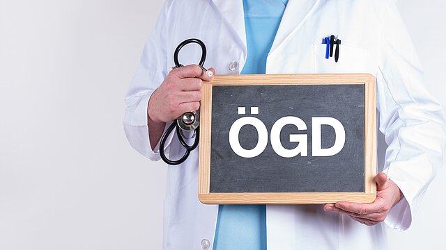Arzt mit einer Tafel auf der ÖGD für den Öffentlichen Gesundheitsdienst steht