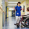 Ärztin erklärt im Krankenhausflur etwas einer älteren Patientin, die im Rollstuhl sitzt
