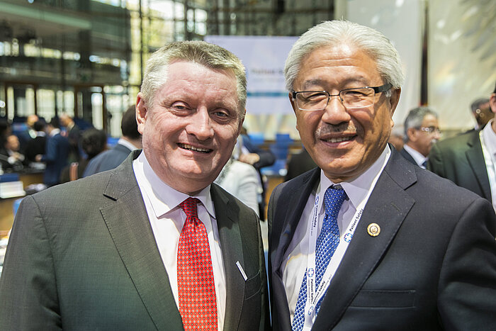 Foto: Hermann Gröhe und Victor J. Dzau stehen nebeneinander im Sitzungssaal und lächeln in die Kamera