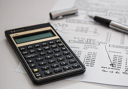 Foto: Taschenrechner und Stift auf einem Blatt mit Kalkulationen