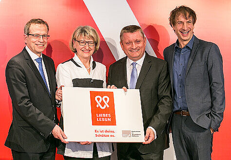 Foto: Bundesgesundheitsminister Hermann Gröhe, der Direktor des Verbands der Privaten Krankenversicherung e. V. Dr. Volker Leienbach, die Leiterin der BZgA Dr. Heidrun Thaiss und Moderator Ingolf Lück halten das Motiv der LIEBESLEBEN-Kampagne in die Kamera.