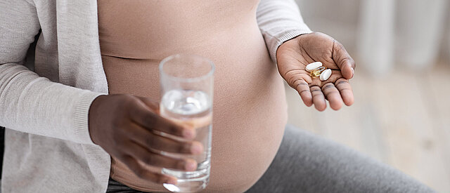 Schwangere Frau mit Wasserglas und Medizin