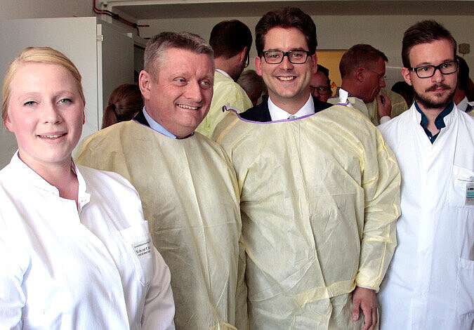 Foto: Bundesgesundheitsminister Gröhe steht neben Prof. Schmeißer und weiteren Wissenschaftlern in Schutzkleidung in einem Laborraum