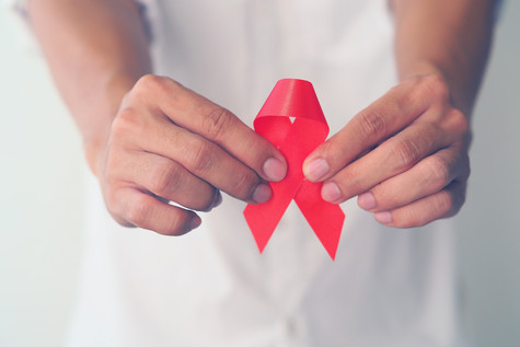 Welt-AIDS-Tag (Bildquelle: Teechai/Shutterstock) Foto: Jemand hält eine rote AIDS-Schleife in die Kamera