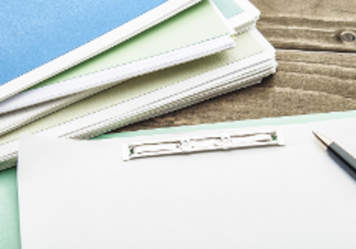 Unterlagen und ein Klemmbrett mit Stift liegen auf einem Tisch