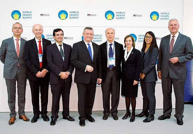 Gruppenfoto mit Bundesgesundheitsminister Gröhe sowie zwei Sprecherinnen und fünf Sprecher aus Wissenschaft, Politik, Wirtschaft und Zivilgesellschaft vor einer Stellwand mit World-Healt- Summit-Logo