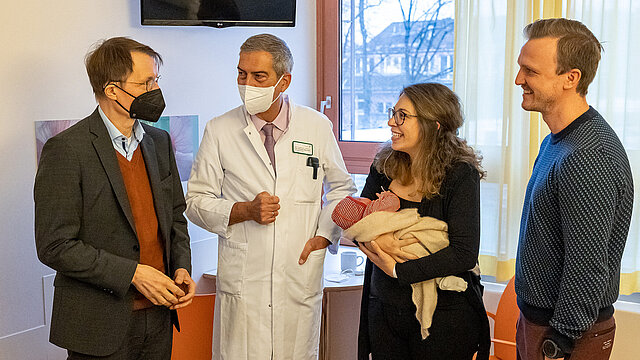 Bundesgesundheitsminister Prof. Karl Lauterbach im Gespräch mit einem Arzt und Eltern mit ihrem neugeborenen Kind