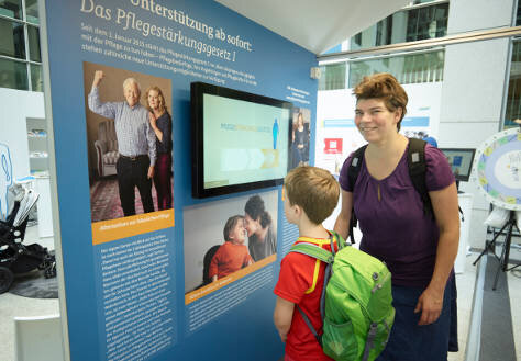 Frau und Junge vor einer Infotafel zum Thema Pflege