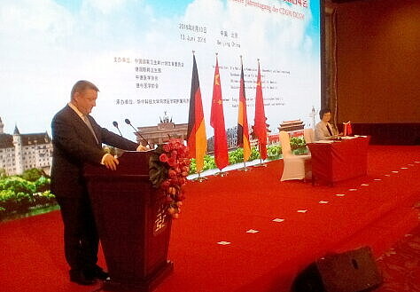 Foto: Bundesgesundheitsminister Hermann Gröhe am Rednerpult; hinter ihm sitzt Li Bin, erste Vorsitzende der Staatlichen Kommission für Gesundheitswesen und Familienplanung