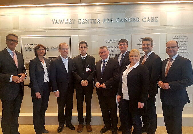 Foto: Gruppenfoto mit Minister Gröhe im Yawkey Center for Cancer Care, dessen Name in silberfarbenen Buchstaben auf der weißen Steinwand hinter der Gruppe zu lesen ist