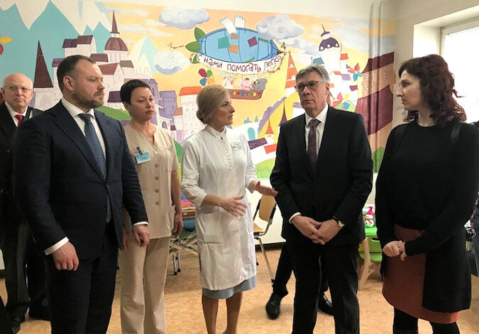 Foto: Eine Ärtzin erklärt der Gruppe etwas in einem Krankenzimmer, die Wände sind bemalt.