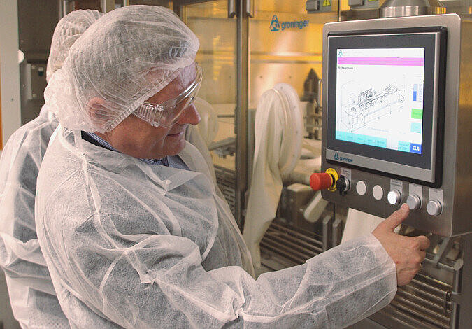 Foto: Bundesgesundheitsminister Gröhe in einem weißen Schutzanzug und bedient einen Monitor; im Hintergrund ein Laborraum mit Glastür