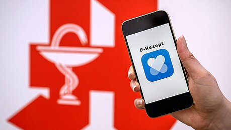 Symbolbild zum E-Rezept - Smartphone vor dem rote Apotheken-A