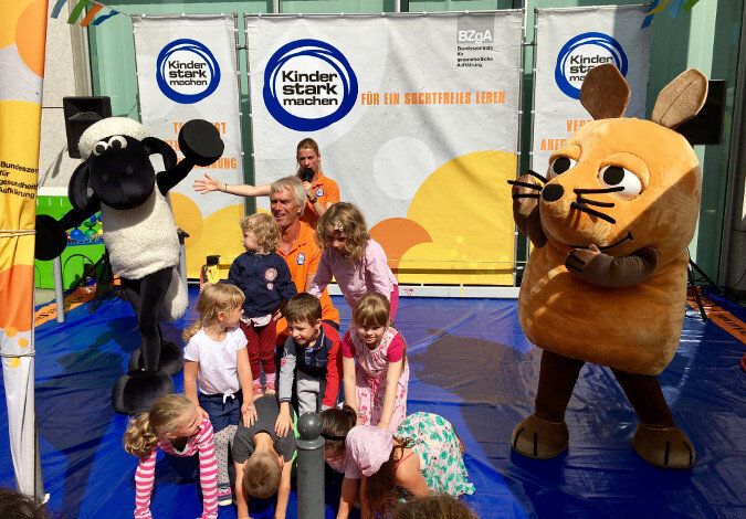 Foto: Kinder bilden eine Pyramide neben dem Ministerium, daneben stehen Shaun das Schaf und die Maus aus der Sendung mit der Maus