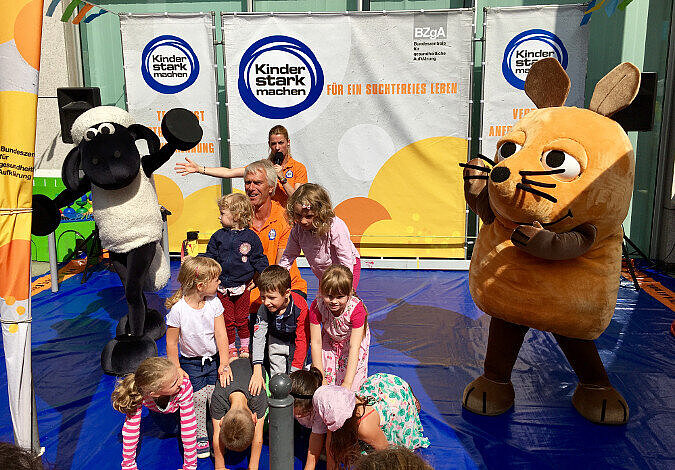 Foto: Kinder bilden eine Pyramide neben dem Ministerium, daneben stehen Shaun das Schaf und die Maus aus der Sendung mit der Maus