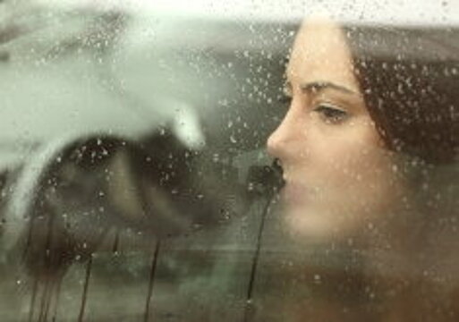 Ein Frau schaut aus einem beschlagenem Autofenster während es regnet.