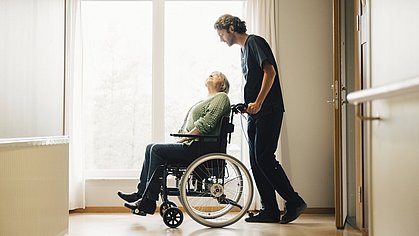 Pfleger mit Frau im Rollstuhl in einem Pflegeheim