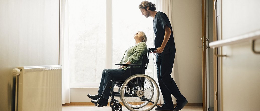Pfleger mit Frau im Rollstuhl in einem Pflegeheim